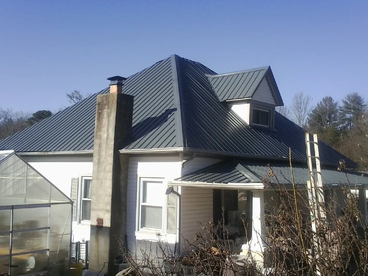 Dark blue standing seam metal roof on a white farmhouse with dormer — Slate & Tile Roof Repair by Roofing Brothers in Homer