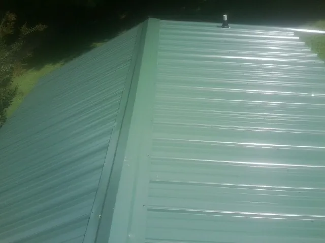 New green metal panels meeting at the ridge of a roof — Flat Roof Repair work by our crew in Homer
